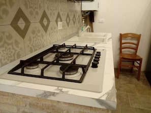Une cuisine équipée d’une cuisinière à gaz, d’un évier et d’une chaise.