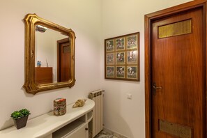 A bathroom with a white vanity, a gold-framed mirror, a potted plant, a decorative box, and a wooden door with a decorative panel.