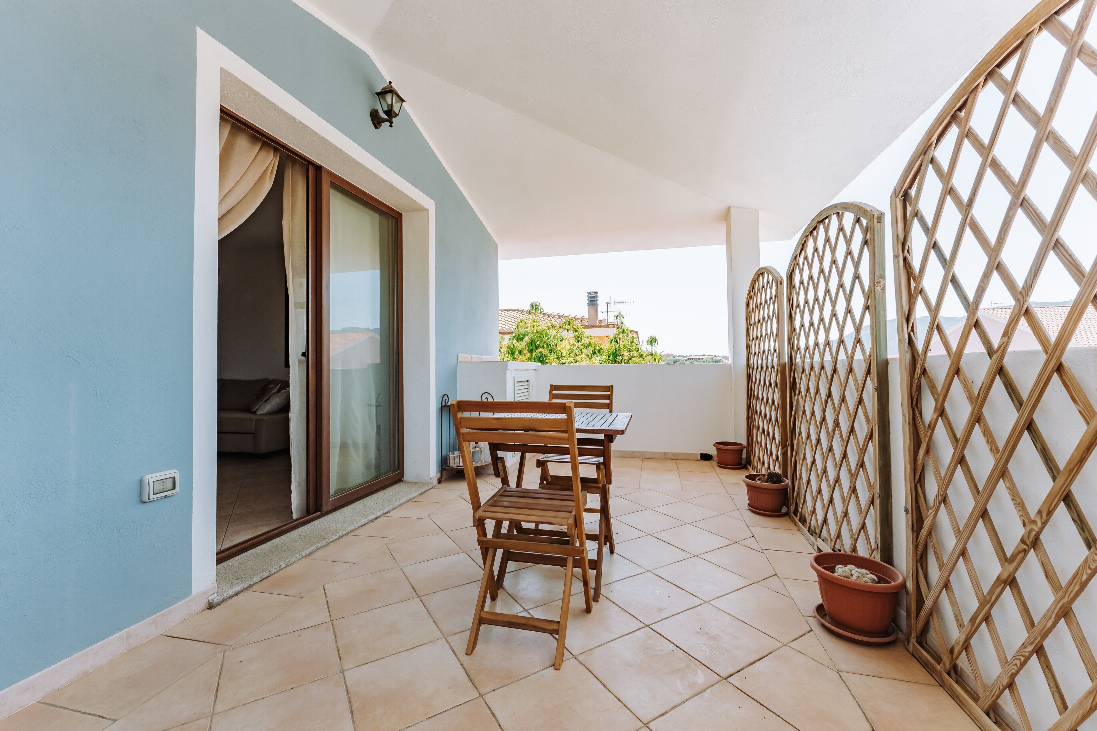 Un balcon avec une table et des chaises, une porte-fenêtre coulissante et une vue sur les bâtiments au loin.