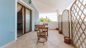 Un balcón con mesa y sillas, una puerta corredera de vidrio y vistas a edificios distantes.