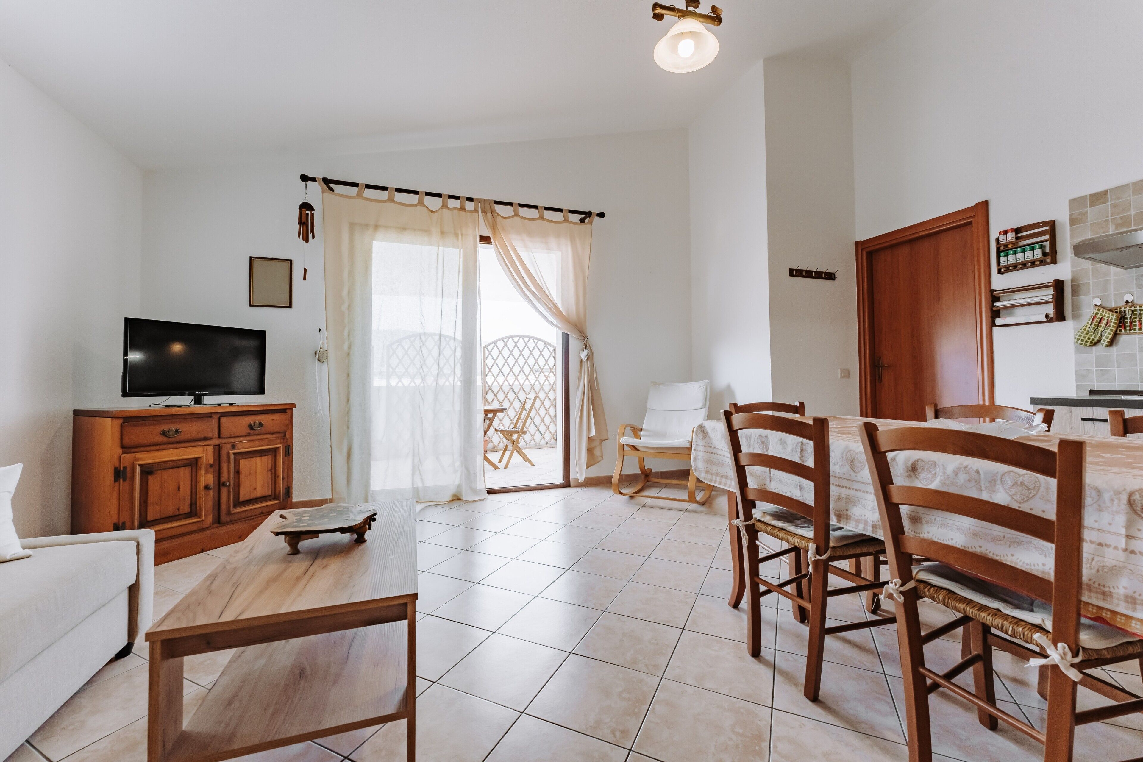 Un salon équipé d’un téléviseur, de meubles en bois, d’un coin repas avec des chaises et une table, et d’une cuisine avec des placards et un comptoir.