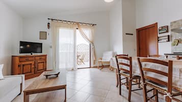 Un salon équipé d’un téléviseur, de meubles en bois, d’un coin repas avec des chaises et une table, et d’une cuisine avec des placards et un comptoir.