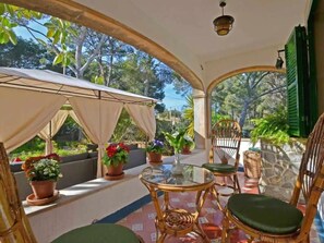 Une terrasse extérieure dotée d’un espace salon couvert, de plantes en pot et offrant une vue sur la verdure environnante.