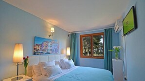 A hotel room with a bed, two bedside lamps, a painting, a window with curtains, and a TV. - Villa 'Benestar' with Private Pool, Wi-Fi, and Air Conditioning (El Toro)