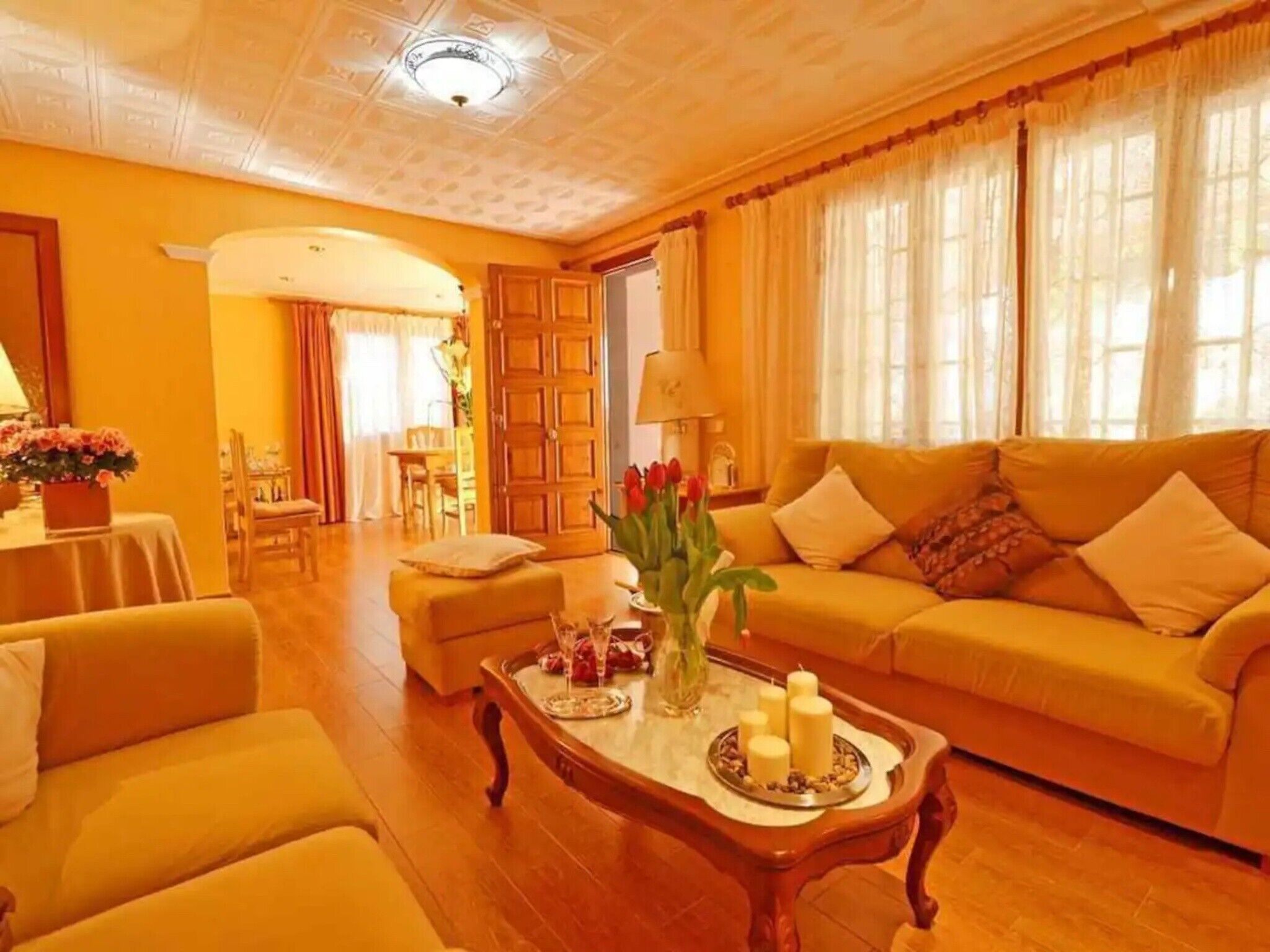 Een woonkamer met een bank, fauteuils, een bijzettafeltje met kaarsen, en een eethoek op de achtergrond.