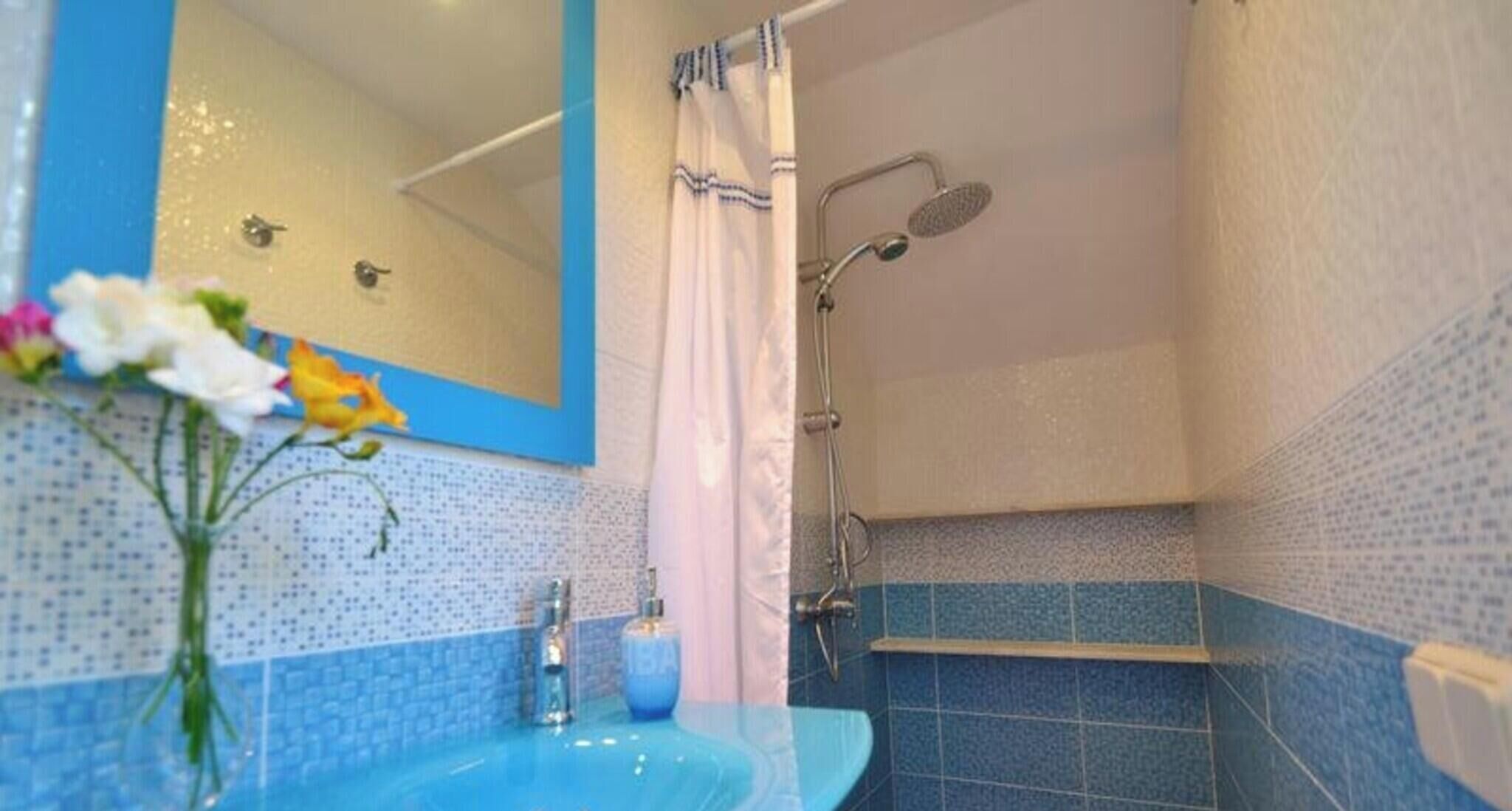A bathroom with a blue tiled wall, a sink, a shower, and a mirror.