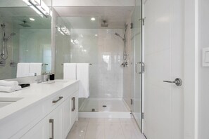 A modern bathroom with a glass-enclosed shower, a white vanity with a large mirror, and a tiled floor.