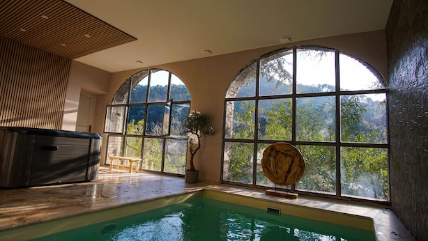 Una piscina interior con grandes ventanales arqueados, un jacuzzi y techo de madera.