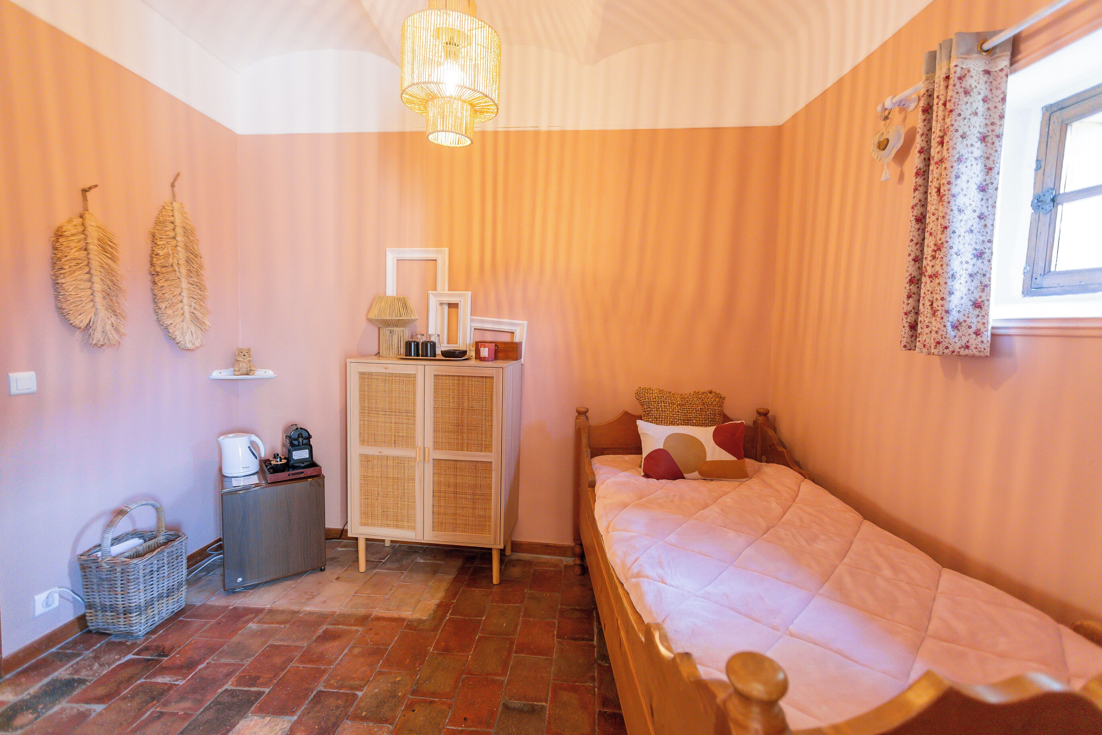 A bedroom with a bed, a chest of drawers, a wicker basket, and a ceiling light fixture.
