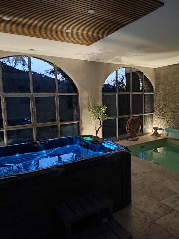 Un espace bien-être comprenant un jacuzzi et une petite piscine, de grandes fenêtres en arc de cercle et un plafond en bois.