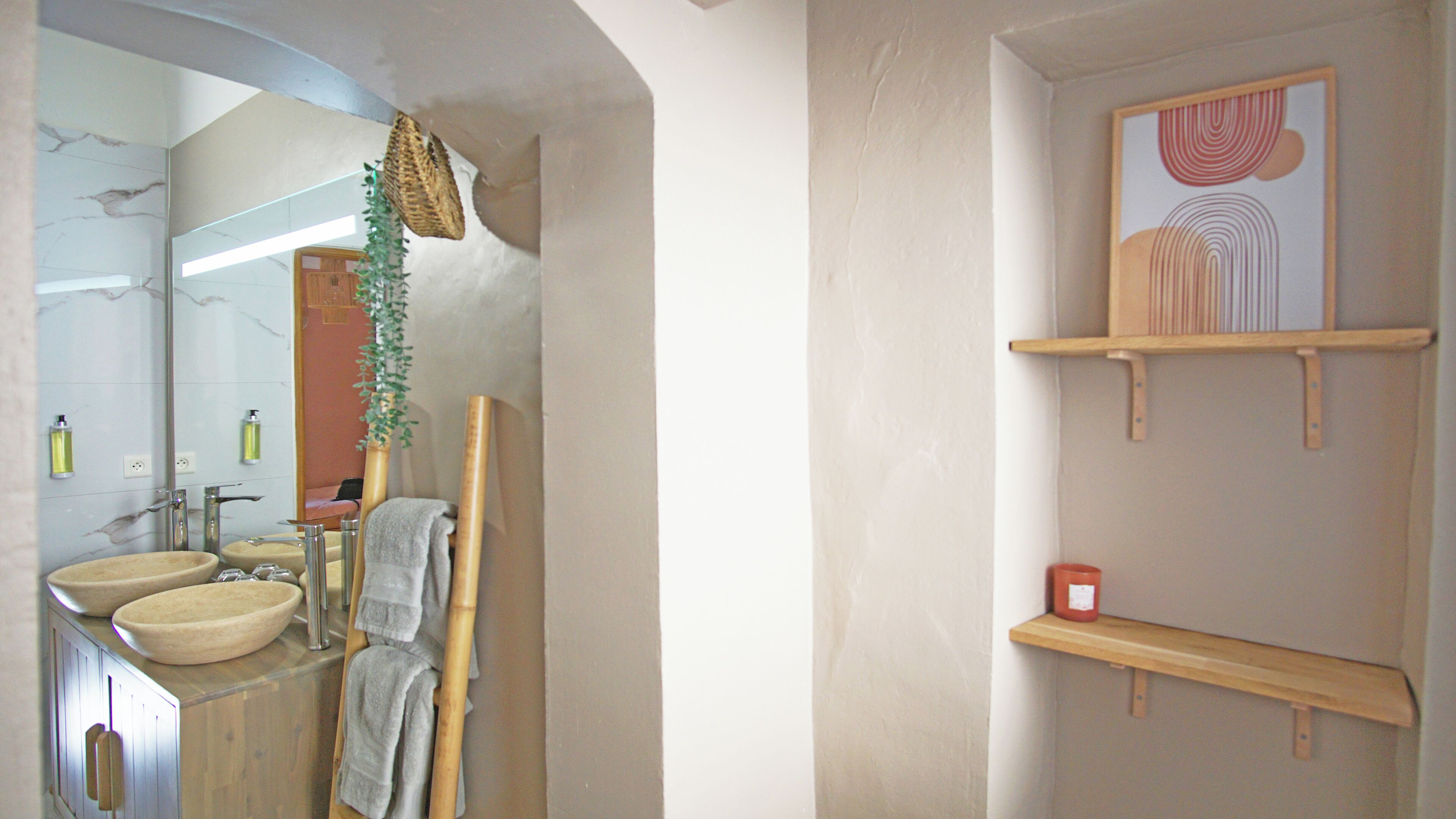 Een badkamer met een marmeren wand, een spiegel, een wastafel, een handdoekhouder en een plank met een fles.