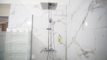Een badkamer met douche, marmeren wanden en een fles shampoo.
