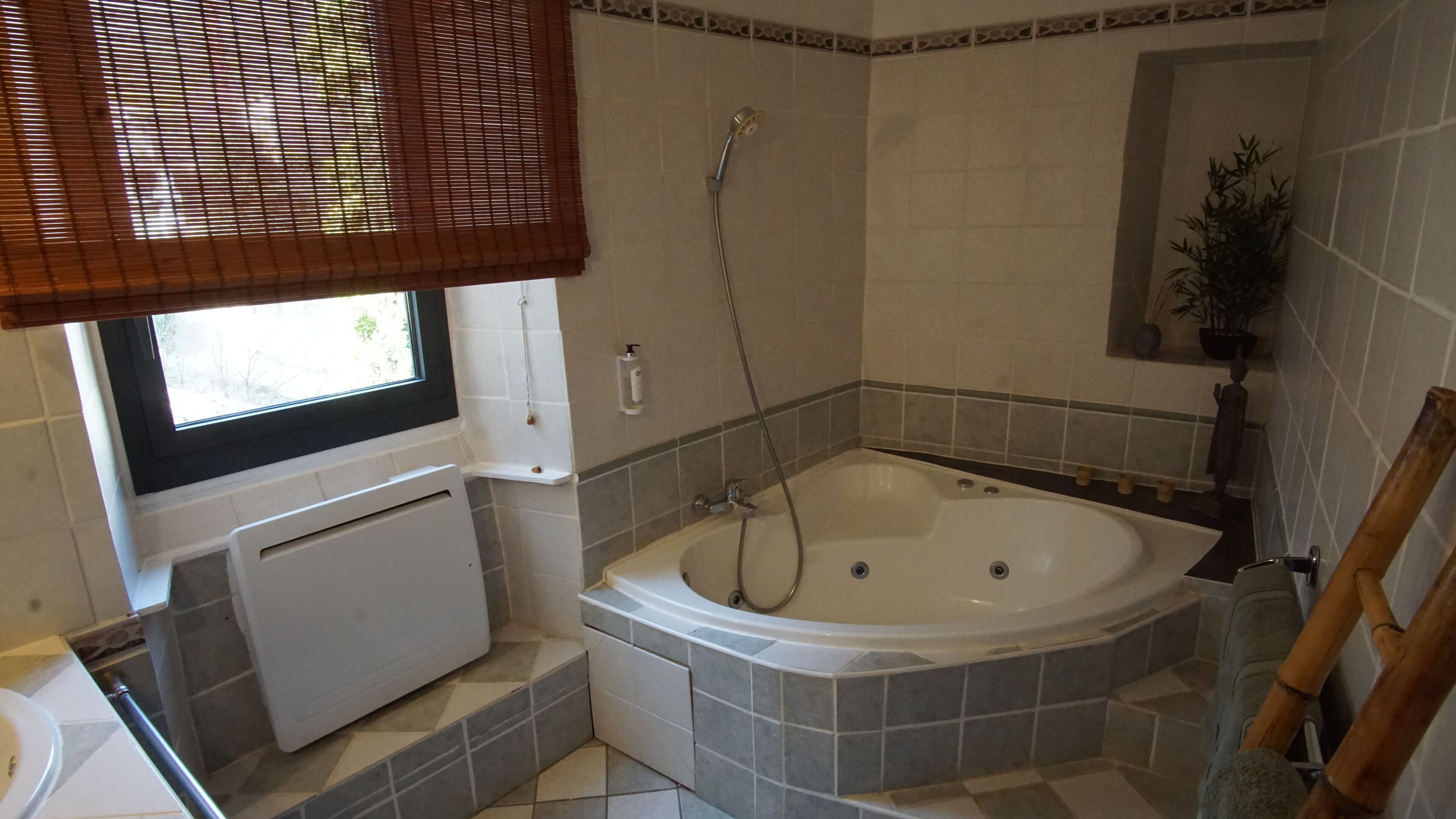 A bathroom with a bathtub, a window with blinds, a radiator, and a shower.