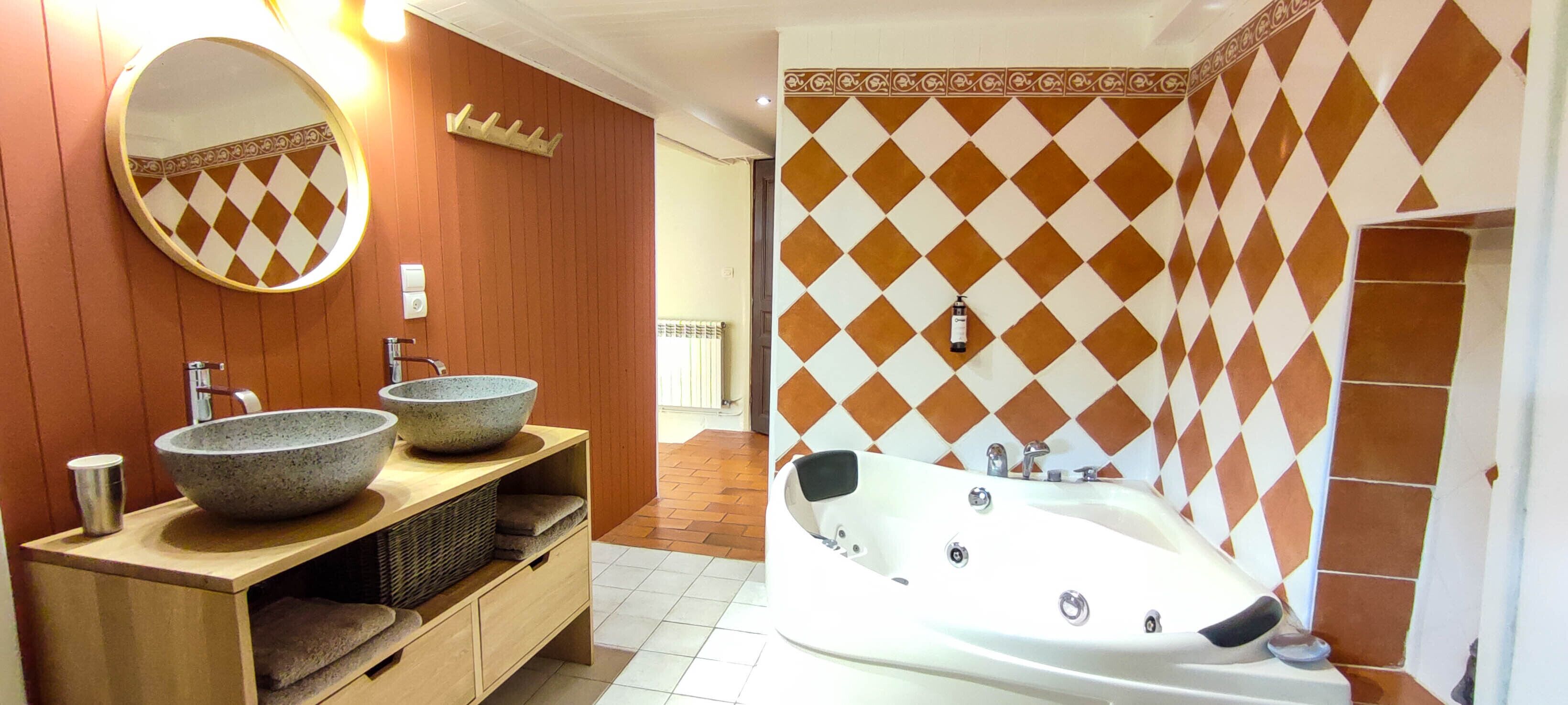 Un baño con tocador de madera, dos grandes lavabos de piedra, un espejo redondo y una bañera blanca.