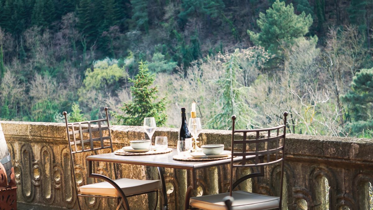 Une table dressée avec des assiettes, des verres et une bouteille, donnant sur une colline boisée.