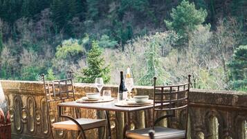 A table set with plates, glasses, and a bottle, overlooking a forested hillside.