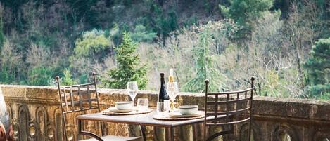 Une table dressée avec des assiettes, des verres et une bouteille, donnant sur une colline boisée.