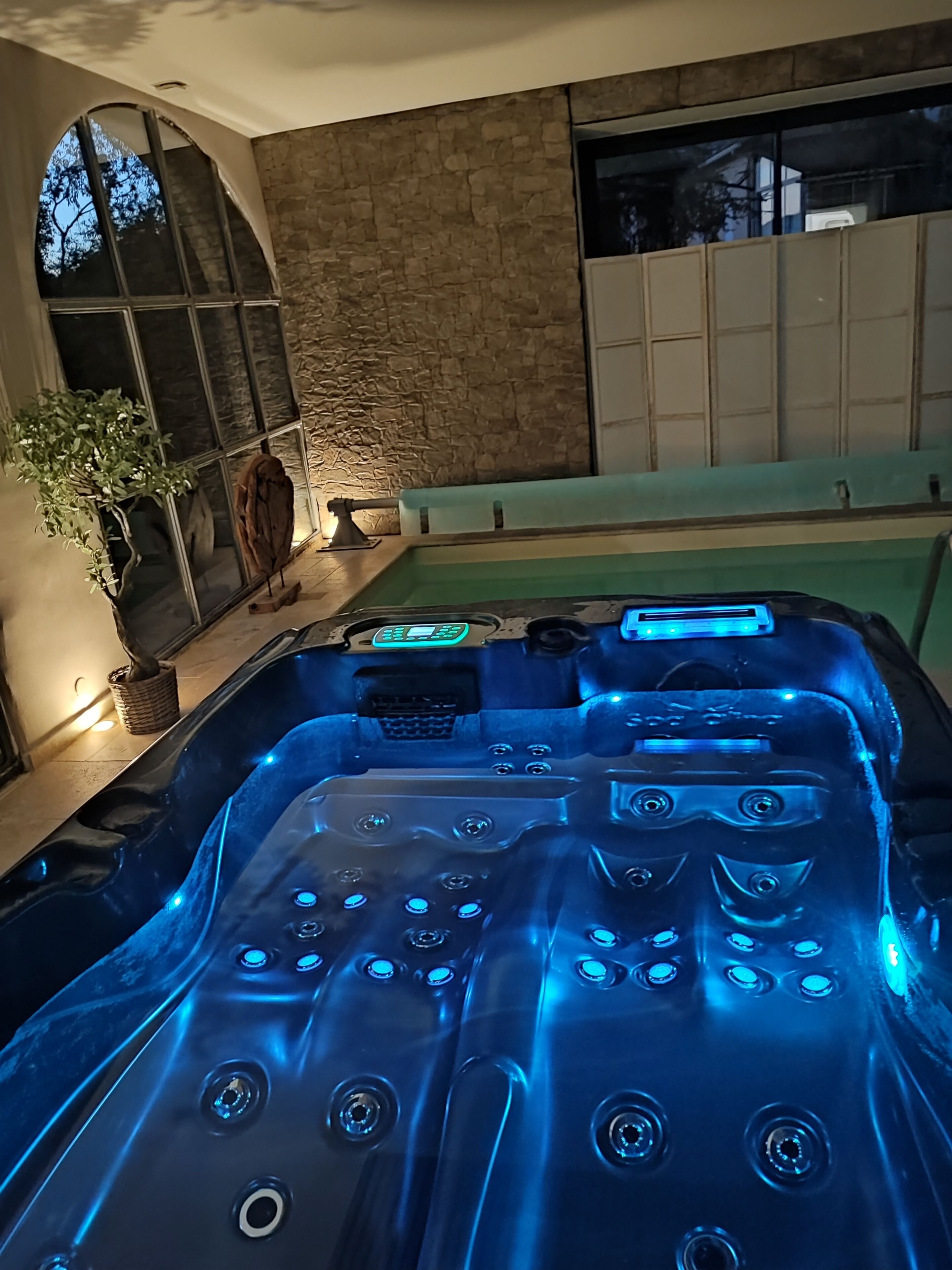 Ein Whirlpool mit blauen LED-Leuchten, einer Steinwand und einem großen Fenster.
