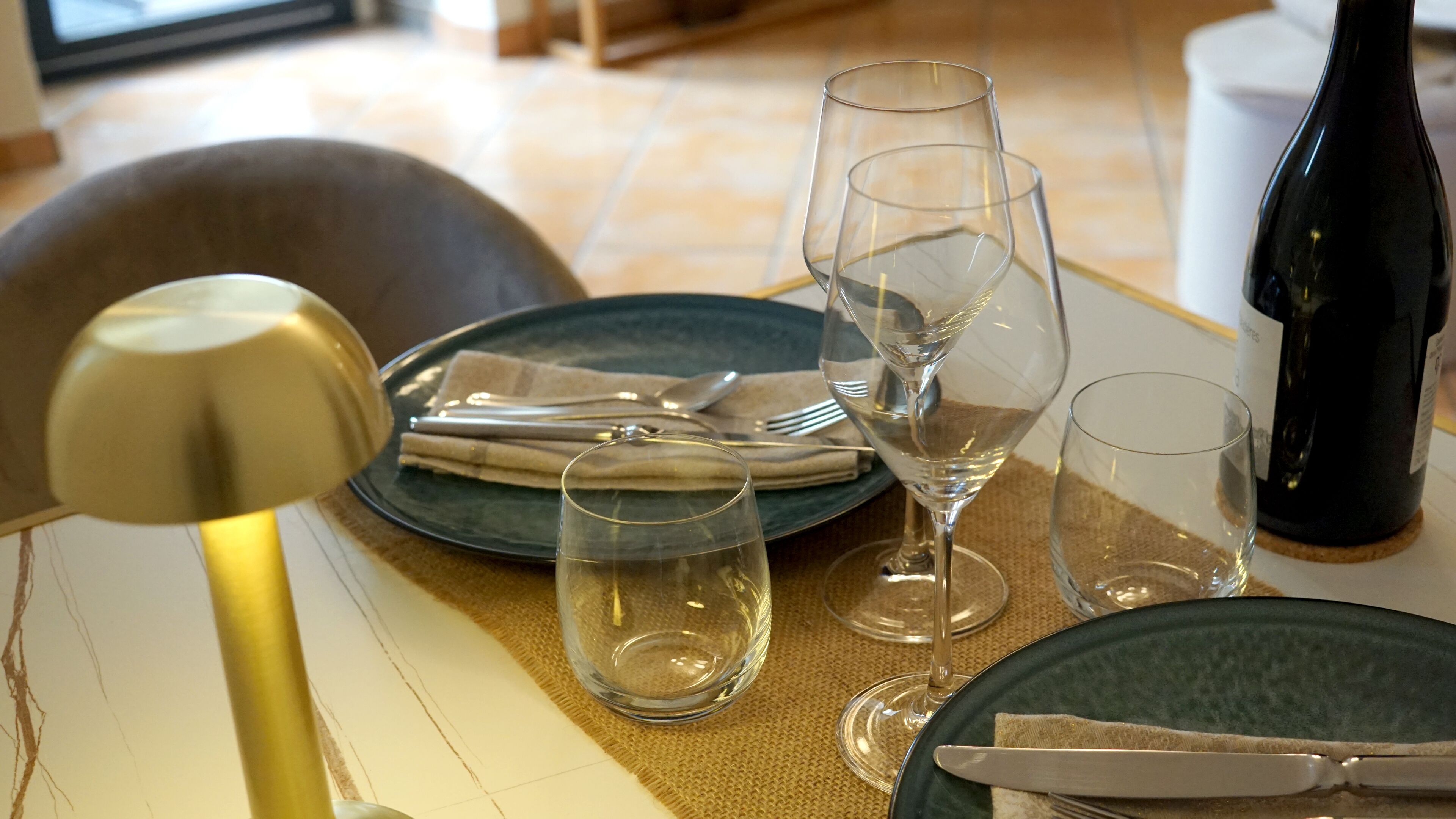A dining table set with plates, glasses, cutlery, and a bottle.
