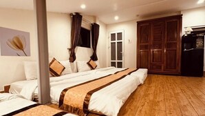 Habitación de hotel con tres camas, piso de madera, un armario y una pequeña cocina.