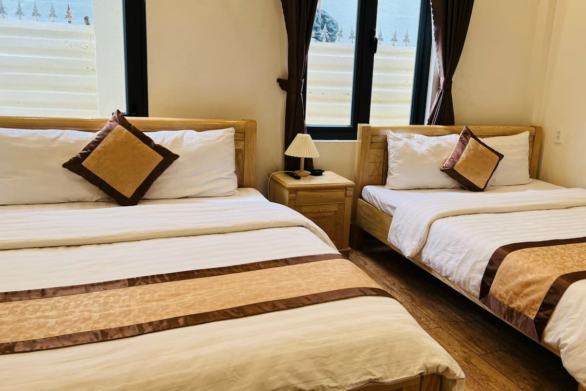 Two single beds with wooden headboards, white bedding, and brown decorative pillows. Each bed has a bedside table with a lamp and a remote control.