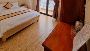 Un dormitorio con cama, un escritorio de madera, una ventana con cortinas y vistas a edificios.