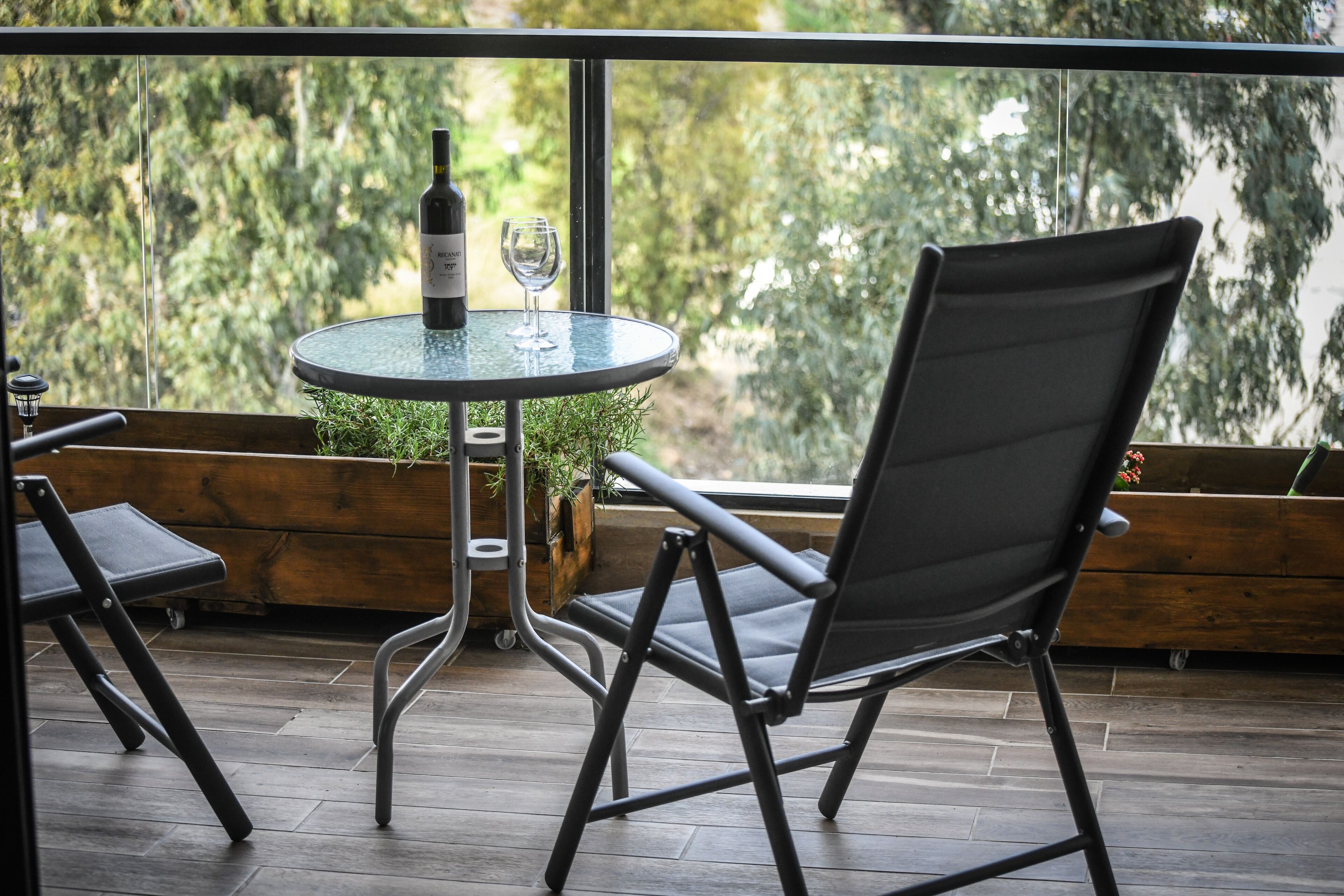 A modern outdoor seating area with a glass table, a wine bottle, and a glass.