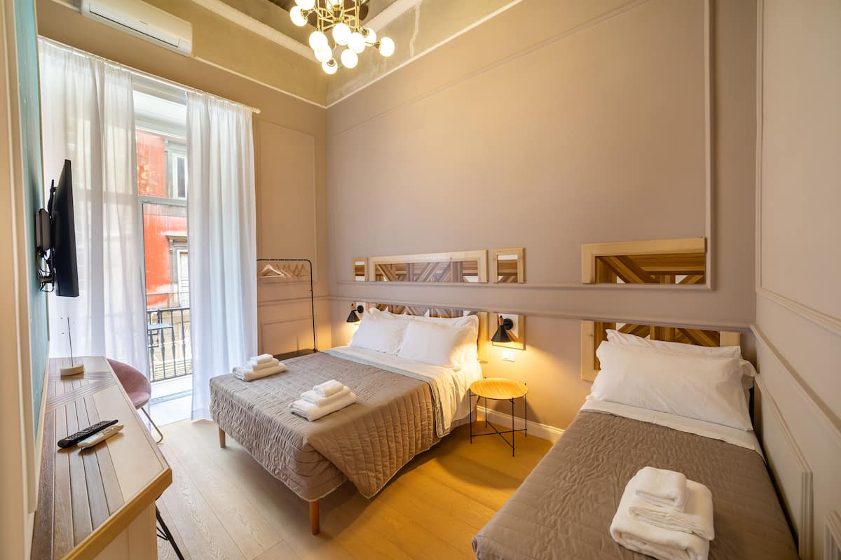 Une chambre d’hôtel avec deux lits, un bureau, une chaise et un balcon donnant sur un immeuble rouge.