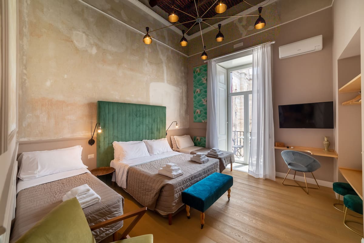 Une chambre d’hôtel avec deux lits, un bureau, une télévision et un balcon avec des rideaux.
