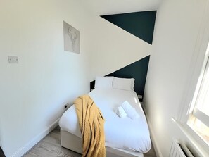 Relax in a serene bedroom with a neatly made bed, dark accent wall, and simple aesthetic.