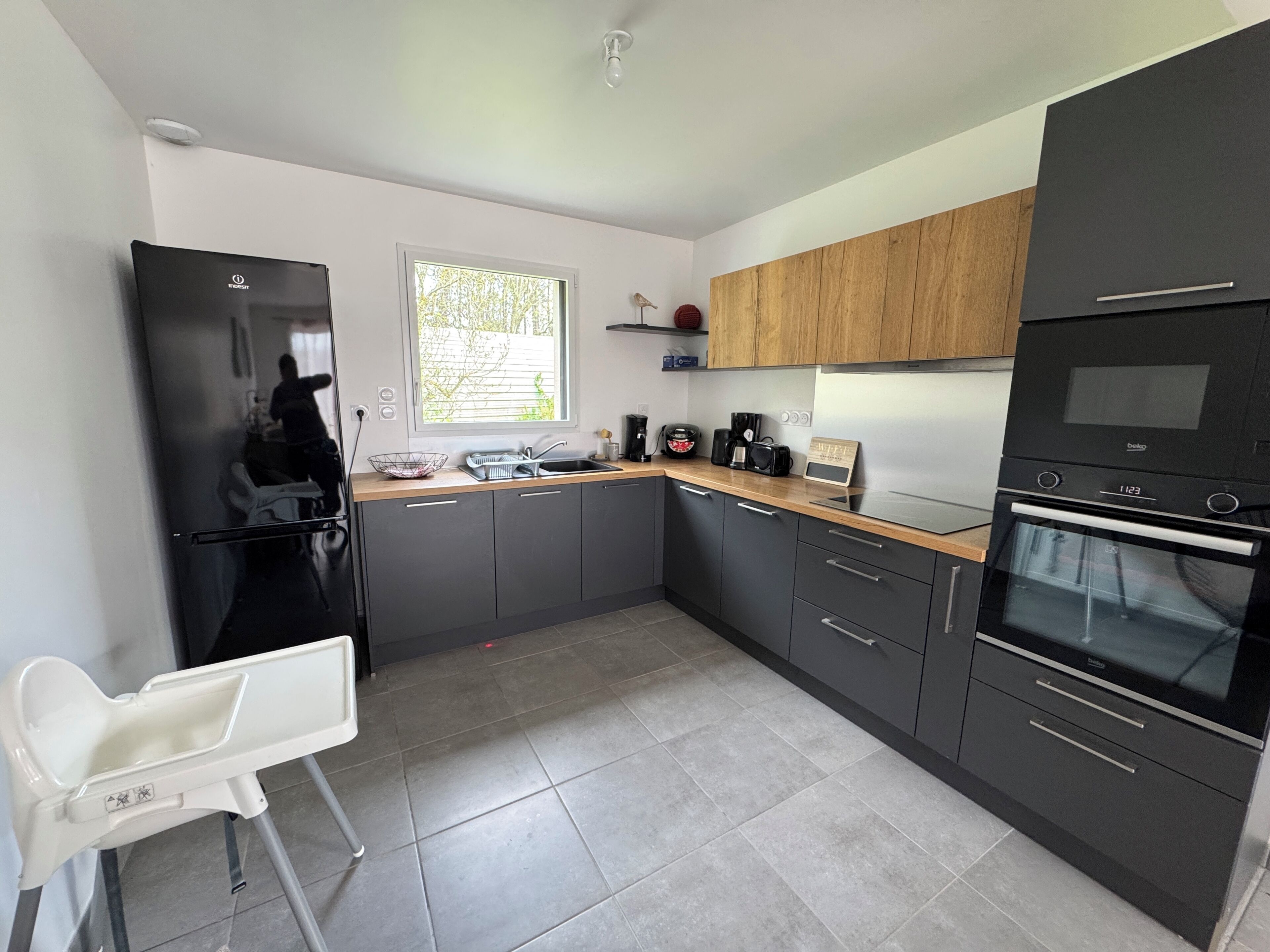 A modern kitchen with a refrigerator, oven, and microwave. There is a window providing natural light.