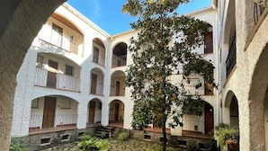 A courtyard with stone flooring, a central tree, and white buildings with balconies. - **Cozy Seaside Studio with Balcony, 200m from Beach, Sleeps 4** (Argelès-sur-Mer)