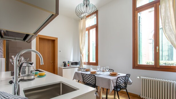 A modern kitchen with a sink, stove, and dining area with a table set for four. - Rialto Bridge Lovely Apartment (Venice)