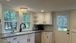A kitchen with white cabinets, a stainless steel dishwasher, a black faucet, a microwave, and a chandelier.