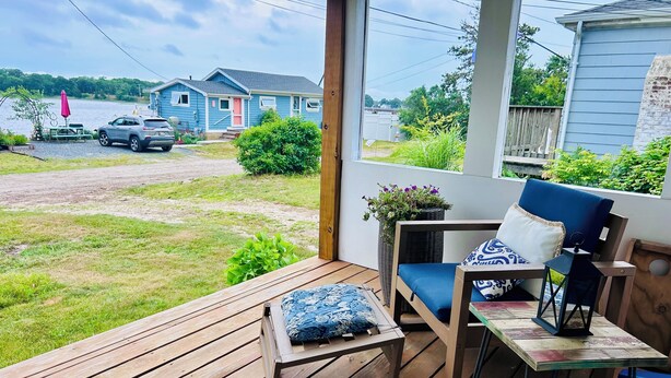 A wooden deck with a chair and table, a potted plant, and a view of houses and a road.