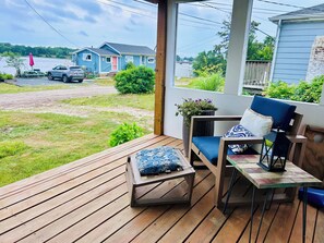 Una terraza de madera con una silla, una mesa, una planta en maceta y vistas a casas y una carretera.