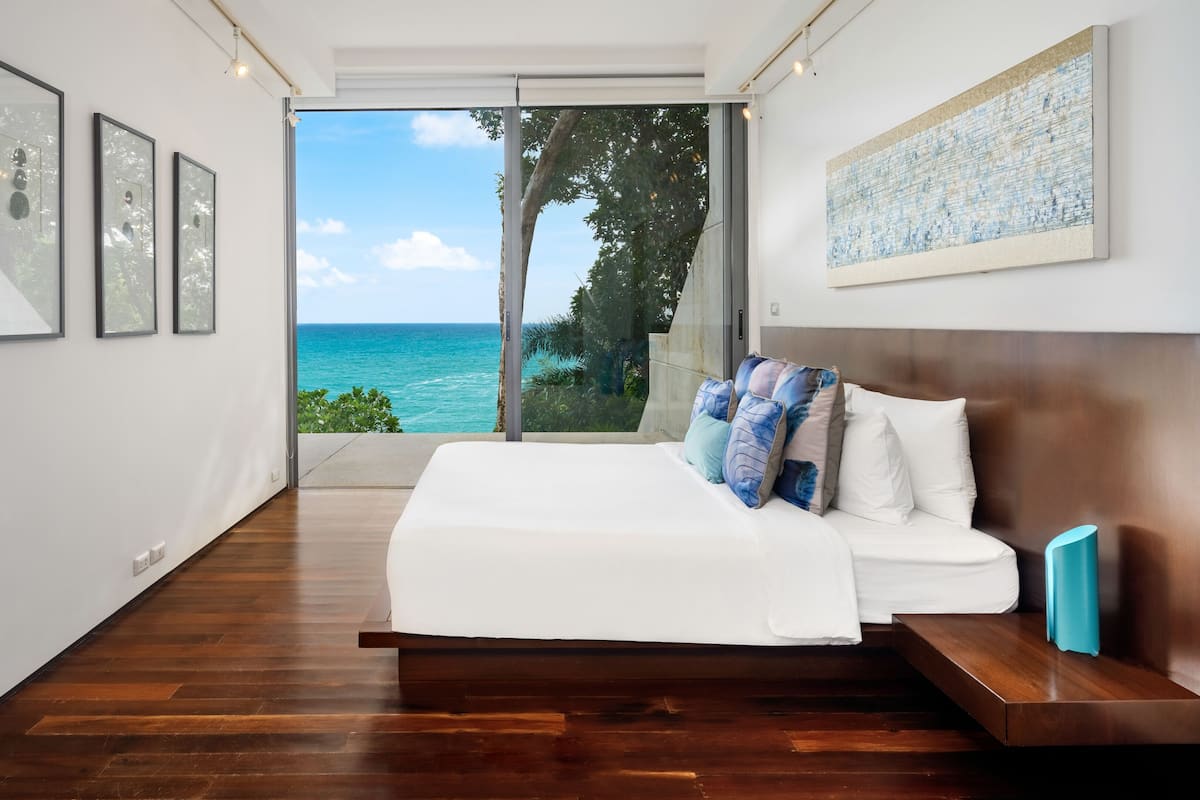 A bedroom with a large bed, a view of the ocean, and framed artwork on the walls.