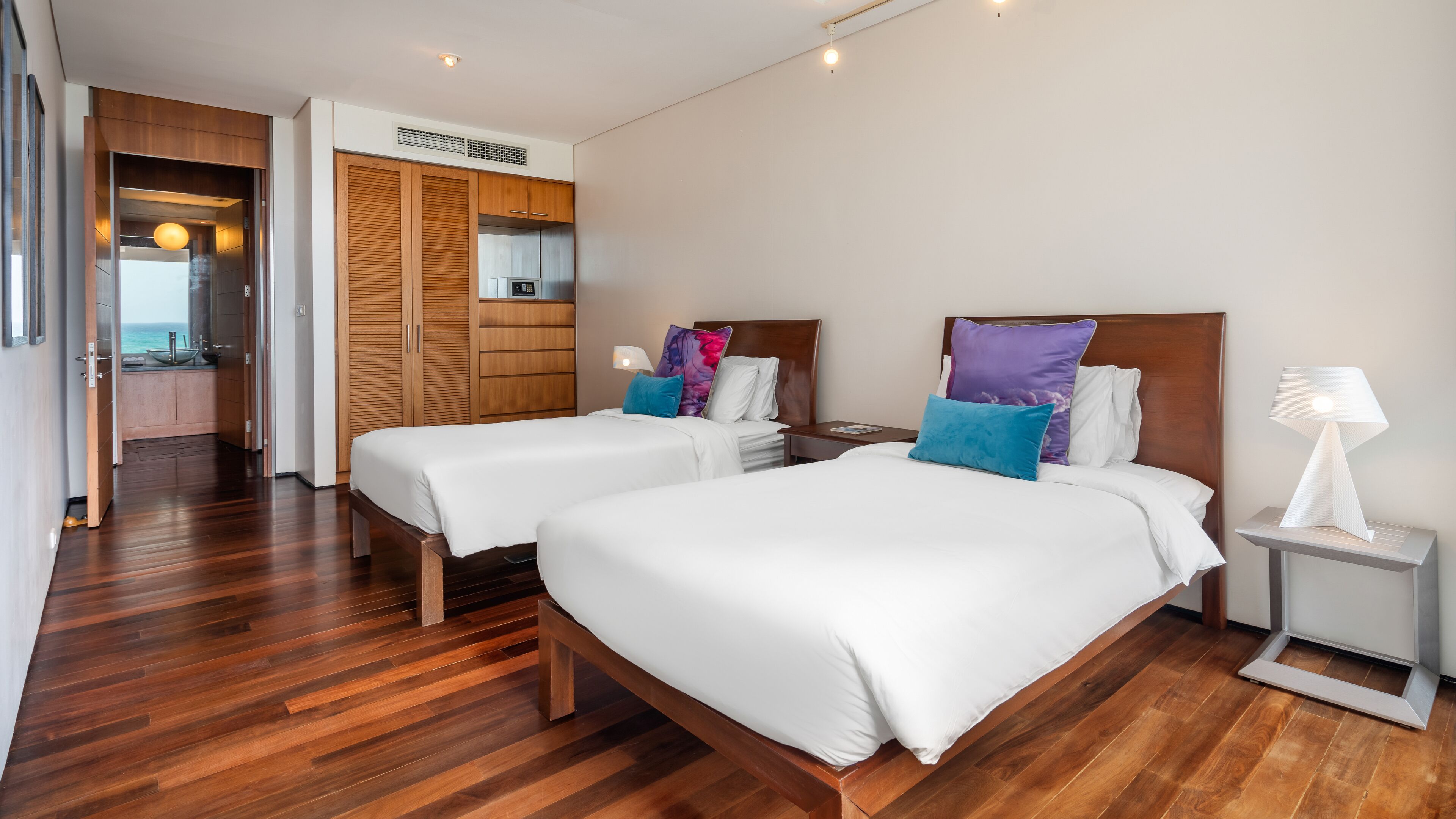 Habitación de hotel con dos camas, suelo de madera, kitchenette y vista al mar.