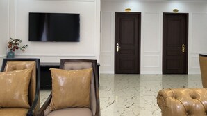 A lobby with a flat-screen TV mounted on the wall, two dark wooden doors, and leather armchairs with cushions. - Golden Sea Hotel (Bai Chay)