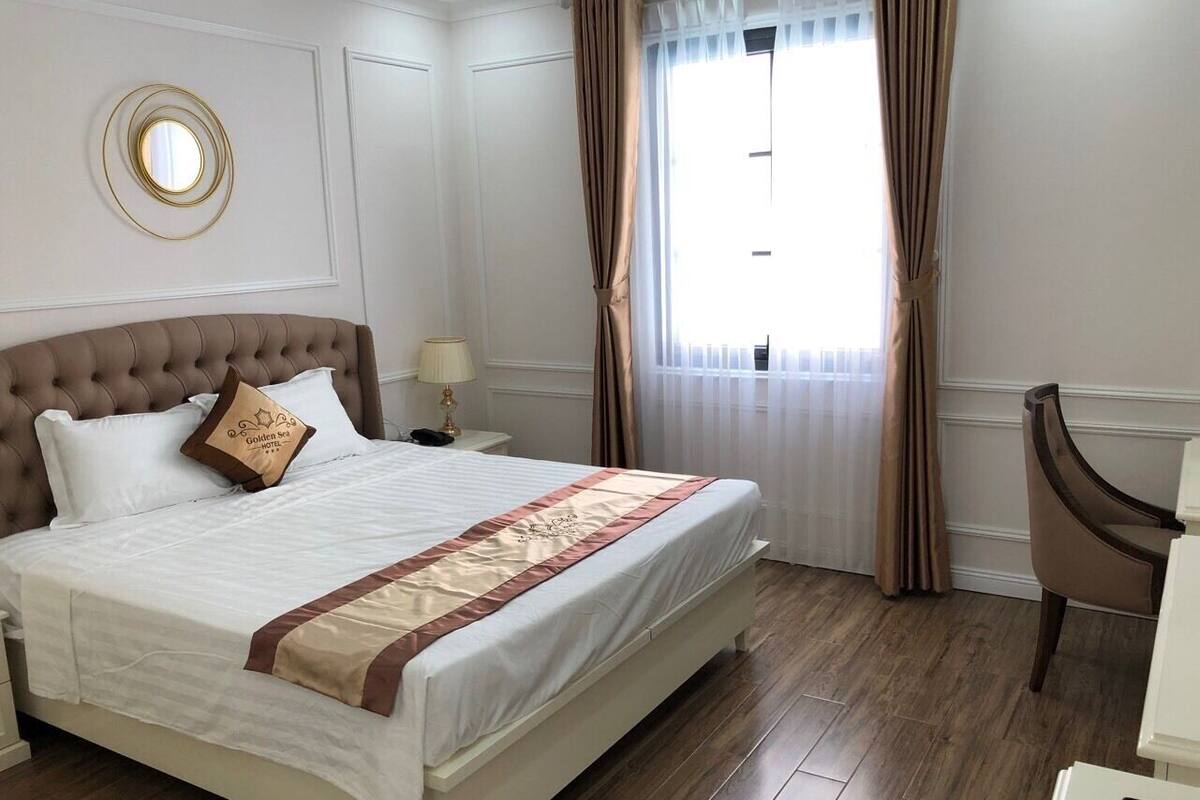 A neatly arranged hotel room with a large bed, a bedside table with a lamp, a chair, and a window with curtains.