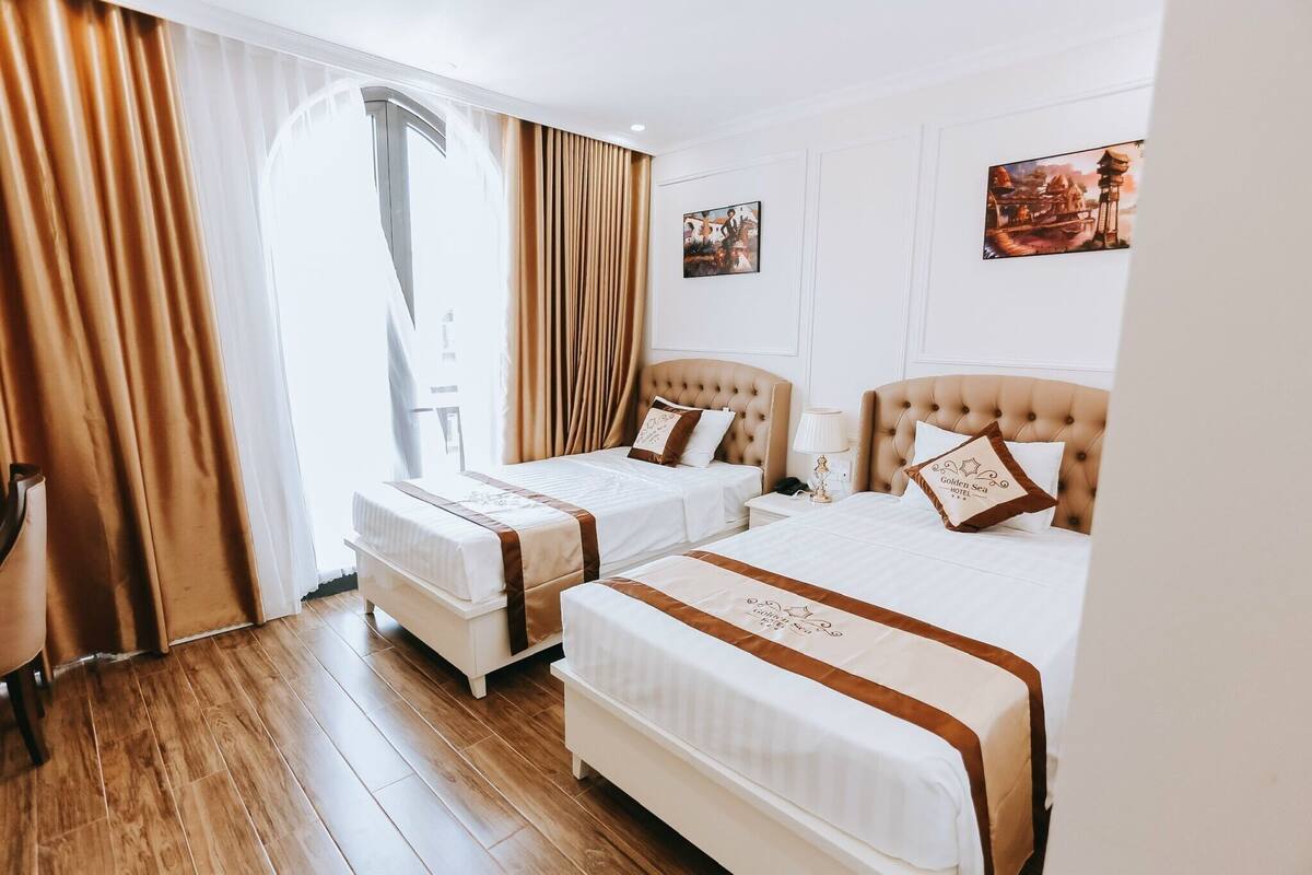 A hotel room with two beds, a wooden floor, and a large window with curtains.