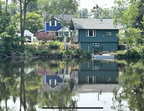 A house with a dock extending into a calm body of water, surrounded by trees and vegetation.