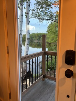 A wooden deck with a railing overlooking a calm lake, surrounded by trees.