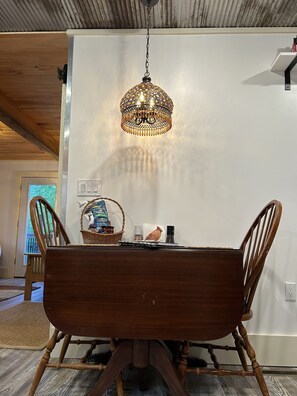 A dining area with a wooden table and chairs, a hanging chandelier, and a basket of snacks on the table.