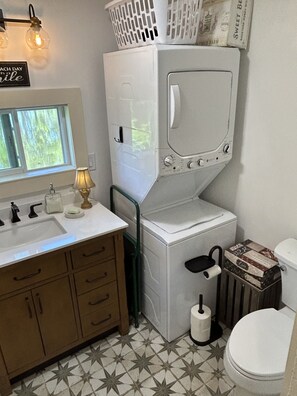 A compact bathroom with a sink, toilet, and a wall-mounted laundry machine.