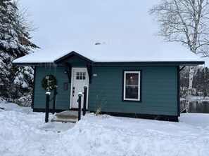 Cozy home with a small porch and a single window, surrounded by a serene winter landscape.