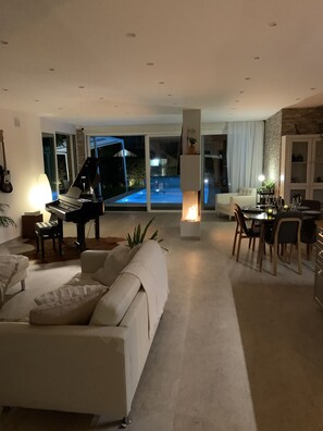 A modern living room with a piano, a sofa, and a dining area with chairs and a table. - Modern Townhouse w Private Pool (Marbella)