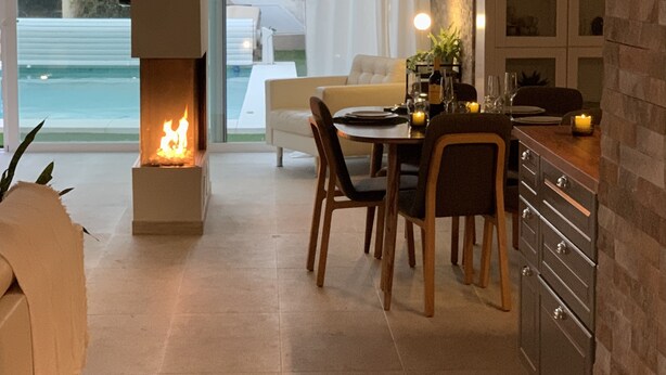Eine moderne Küche mit Kamin, Essbereich und großen Fenstern mit Blick auf einen Pool.