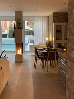 A modern kitchen with a fireplace, dining area, and large windows overlooking a pool. - Modern Townhouse w Private Pool (Marbella)