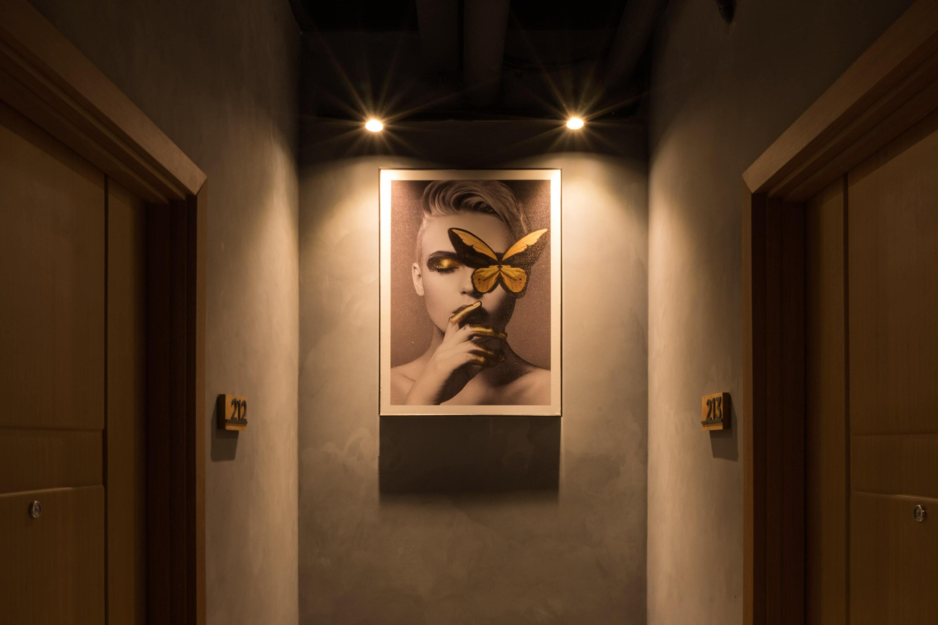 Um corredor com uma obra de arte emoldurada na parede, portas de ambos os lados e uma placa com números acima de cada porta.